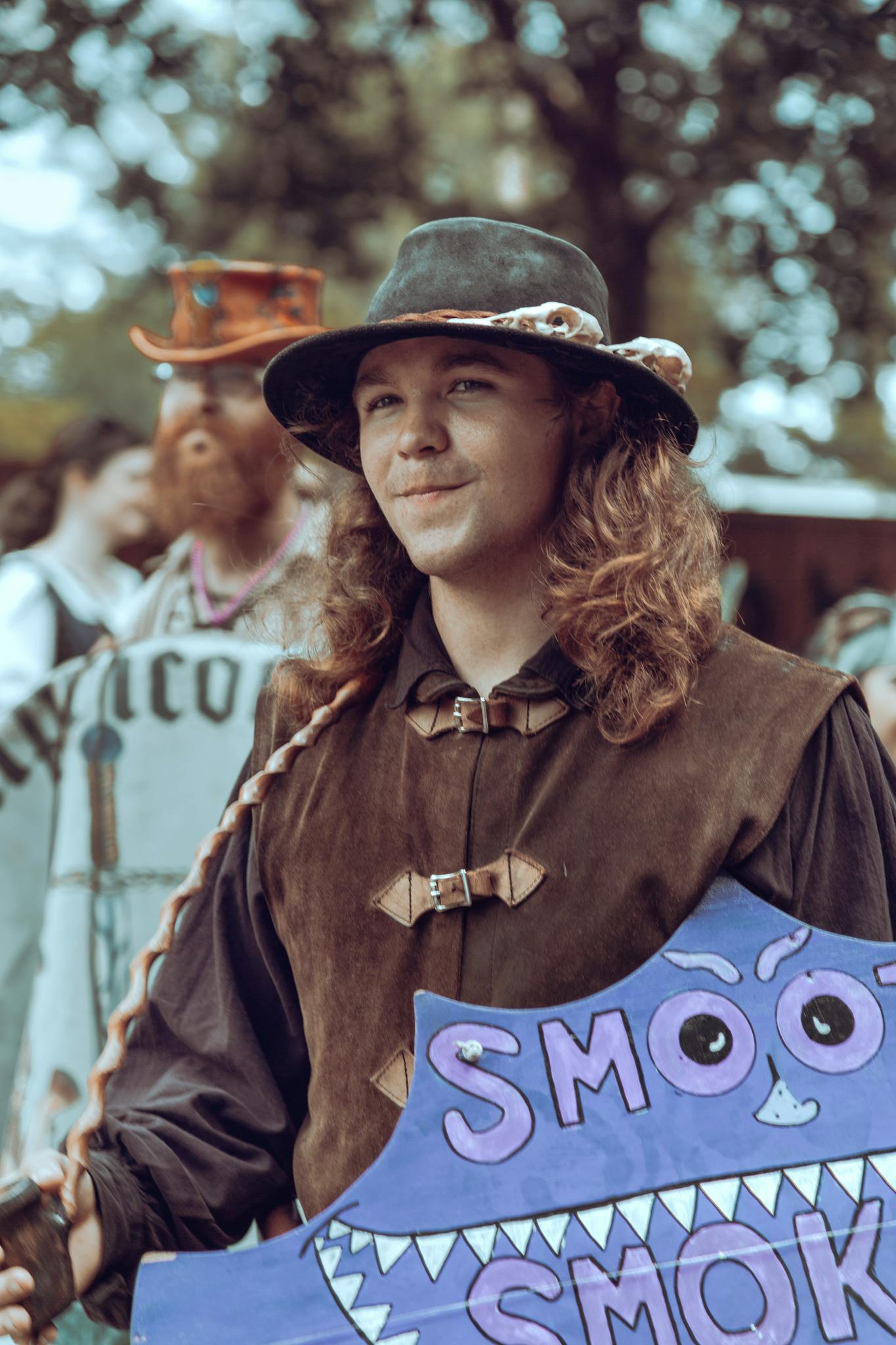 A medieval reenactor in costume holds a colorful shield at an outdoor festival.