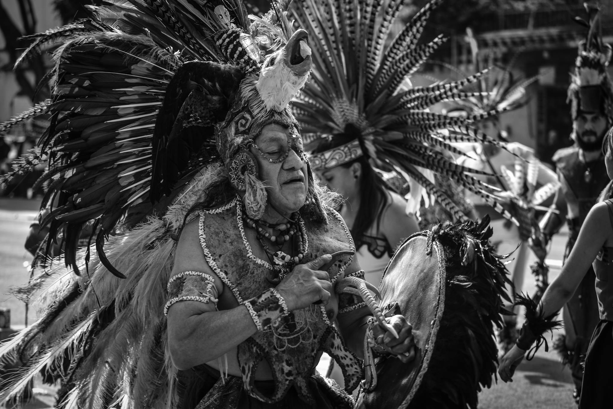 Black and white photo of performers in traditional indigenous attire during a parade in Mexico City.