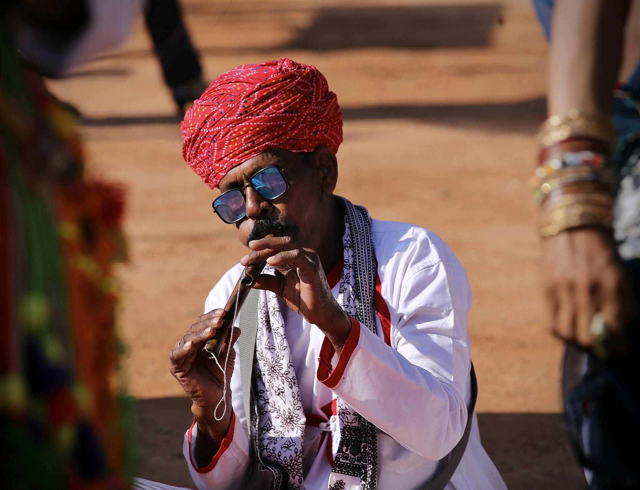 Man in traditional attire plays flute at Indian street performance, vibrant cultural scene.